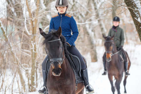 Two young girls riding horse in snowy park in winterの写真素材