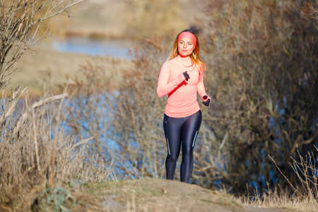 Young woman jogging in the park near the pond in the cold sunny morningの写真素材