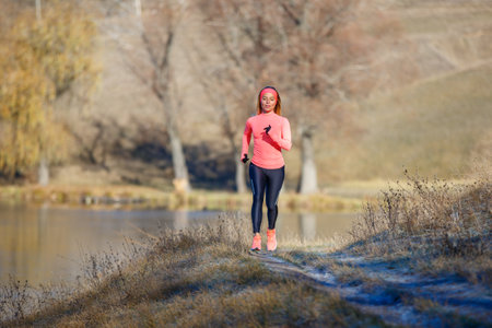 Fitness girl jogging in park near pond in the frosty morning.の写真素材