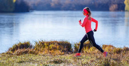 Young slim woman running along the lake in the cold morning