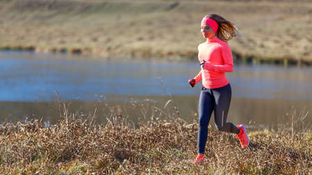 Young slim woman running along the lake in the cold morningの写真素材