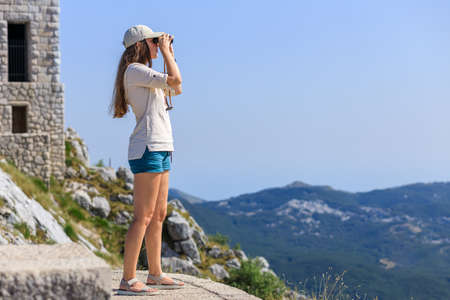 Young woman watching mountain landscape through binoculars at the view spot on tourist trailの写真素材