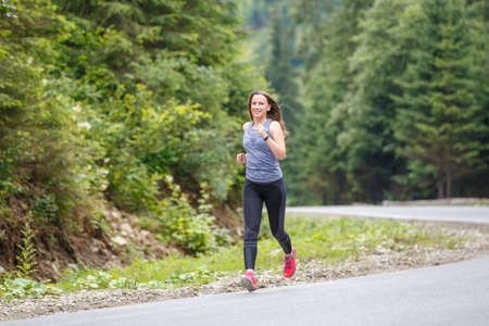 Runner woman running on the mountain road through the forest.