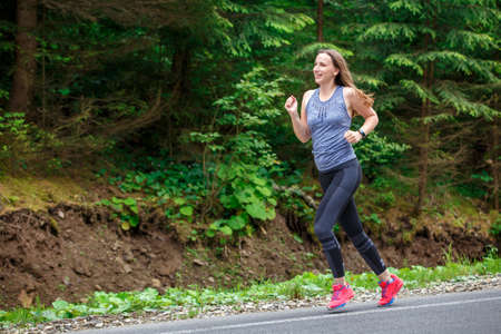 Runner woman running on the mountain road through the forest.の写真素材