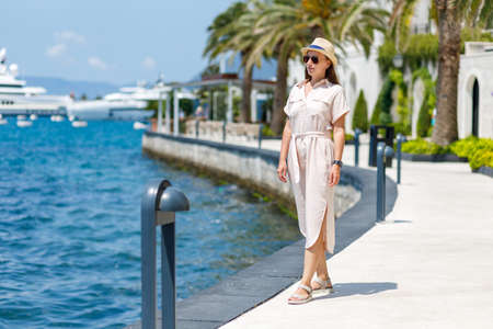 Young lady in dress and hat walking near the marina pierの写真素材