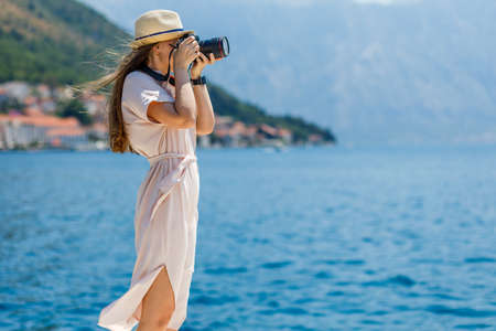 Young travel lady in dress takes photo with professional camera at sunny day