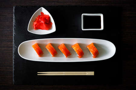 Sushi roll covered with salmon served in long plate on slate boardの写真素材