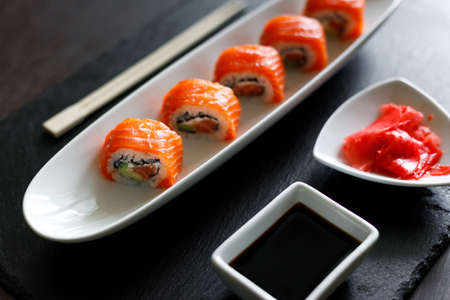 Sushi roll covered with salmon served in long plate on slate boardの写真素材