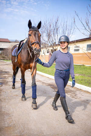Young jockey teen girl walking with the horse before trainingの写真素材