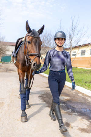 Young jockey teen girl walking with the horse before trainingの写真素材