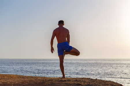 Young man doing yoga practice at the beach in the morningの写真素材