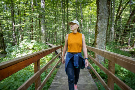 Young woman walking on the bridge on tourist trail in nature parkの写真素材