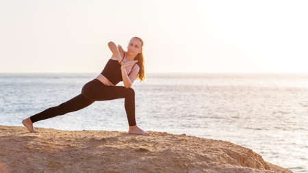 Young fitness woman doing twisting yoga pose at the beach in the morningの写真素材