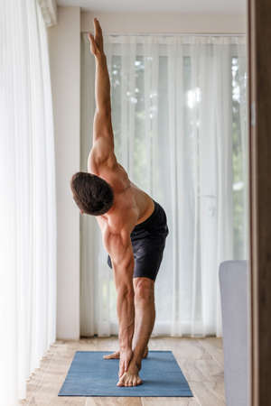 Young fit man doing yoga practice at home in the morningの写真素材
