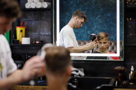 Young male barber arranging haircut of the teenage boy in barbershopの写真素材