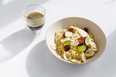 Top view of morning meal on white background. Oatmeal with fruit and cup of coffeeの写真素材