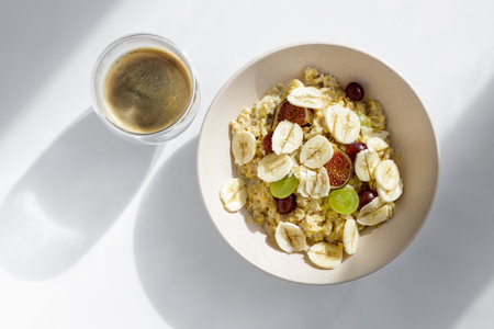 Top view of morning meal on white background. Oatmeal with fruit and cup of coffeeの写真素材