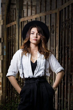 Young woman in white shirt and black hat standing near the gate.の写真素材