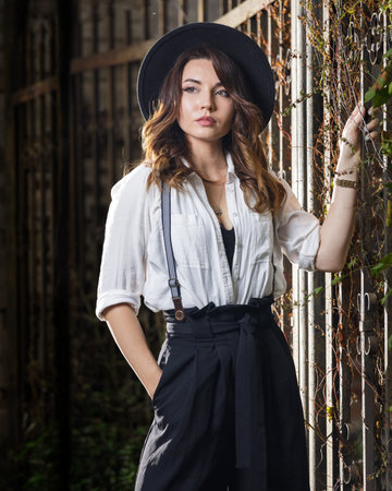 Young woman in white shirt and black hat standing near the gate.の写真素材