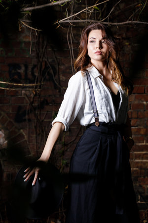 Young woman in white shirt and black hat standing in the darkness.の写真素材