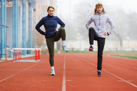 Two young women doing running training stretching legs on the trackの写真素材