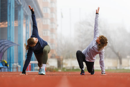 Two young women doing running training stretching legs on the trackの写真素材