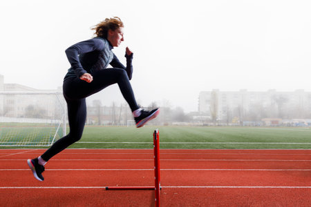 Young sportswoman doing running training with hurdles in the foggy morningの写真素材