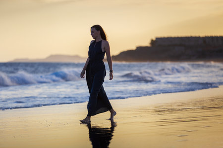 Young beautiful woman in long dress walking at la tejita beach at sunsetの写真素材