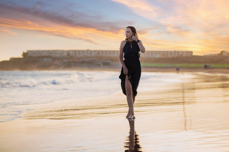 Young beautiful woman in long dress walking at la tejita beach at sunsetの写真素材