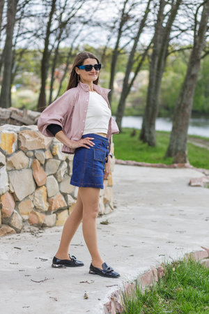 Young woman in pink jacket and denim skirt posing outdoorsの写真素材