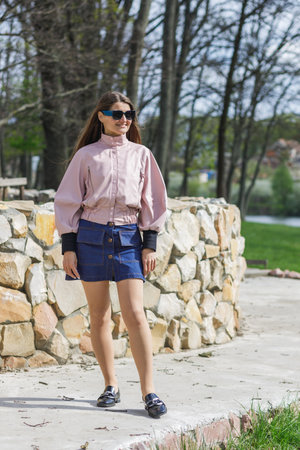 Young woman in pink jacket and denim skirt posing outdoorsの写真素材