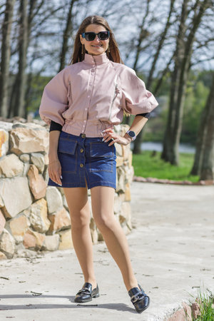Young woman in pink jacket and denim skirt posing outdoorsの写真素材
