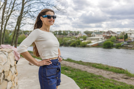 Young woman in short denim skirt and blouse walking along the lakeの写真素材