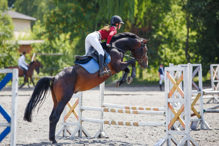 Young woman riding horseback jumping over the hurdle on showjumping courseの写真素材