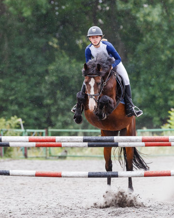Young woman riding horseback jumping over the hurdle on showjumping courseの写真素材