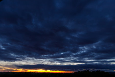 Panoramic sunset sky with heavy dark blue clouds and orange line of sunの写真素材