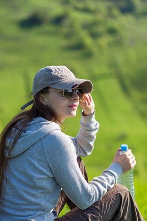Young hiking woman taking a rest at green hill for rehydrationの写真素材