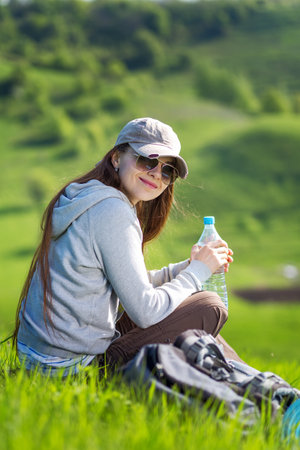 Young hiking woman taking a rest at green hill for rehydrationの写真素材