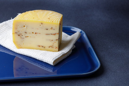 A block of artisan cheese infused with herbs is resting on a white cloth, placed on a blue ceramic serving plate, highlighting its rich textures and colors.の写真素材