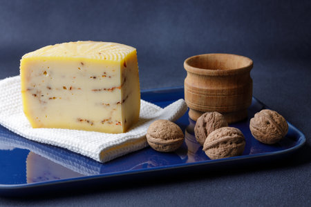 A beautifully arranged platter features a wedge of artisan cheese infused with herbs, surrounded by whole walnuts and a small wooden bowl.の写真素材