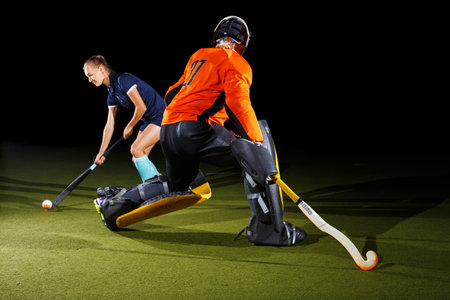 Intense field hockey action between goalkeeper and forward against black backgroundの写真素材