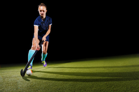Determined young woman skillfully leading the ball with the field hockey stick focused on her game.