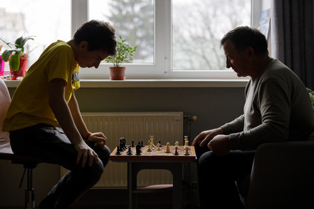 Young boy playing chess with his grandfather indoors during a quiet afternoonの写真素材