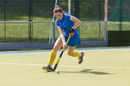Young female player running with the ball in a field hockey matchの写真素材