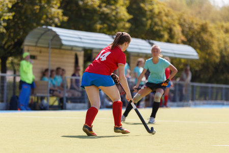 Young women compete in a hockey match on an outdoor field during summerの写真素材