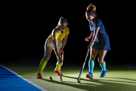 Two field hockey players compete in an intense match under contrast studio lightの写真素材