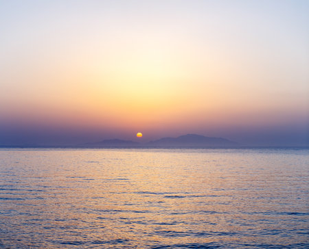 Stunning sunrise over calm sea waters with distant islands in the backgroundの写真素材