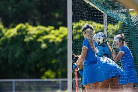 Field hockey players in blue uniforms focus on defending the goal