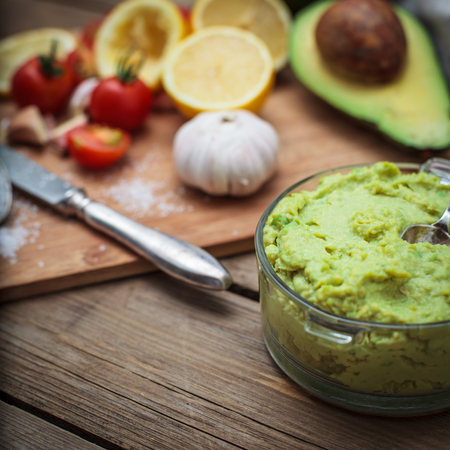 Guacamole on wooden table surrounded by its ingredientsの写真素材