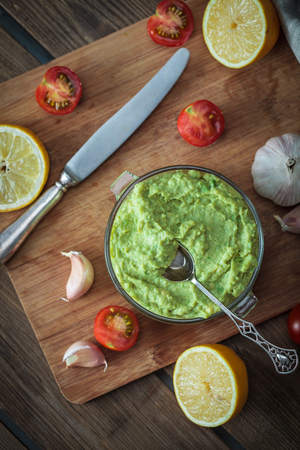 Guacamole on wooden table surrounded by its ingredientsの写真素材